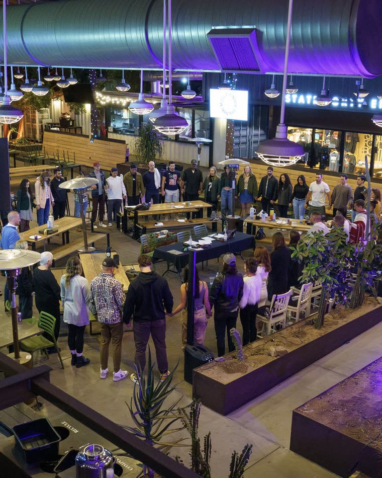 A large mixed group standing in a circle at an outdoor venue
