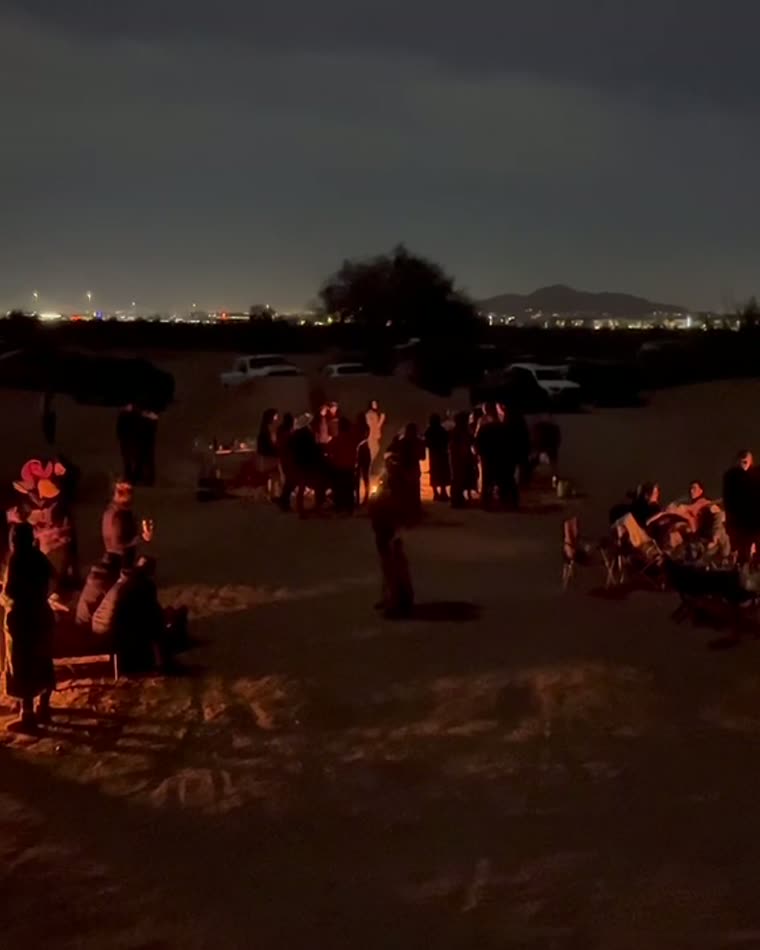 A crowd gathered around fires in the desert at night