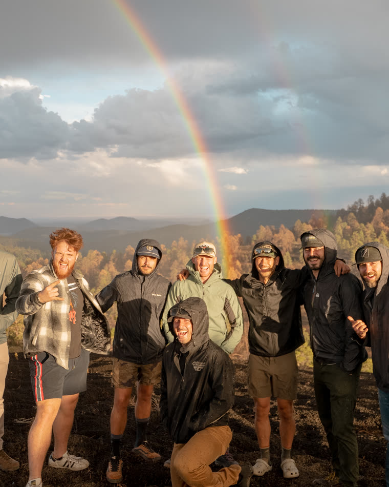 A group of men on a ridge under a rainbow at golden hour