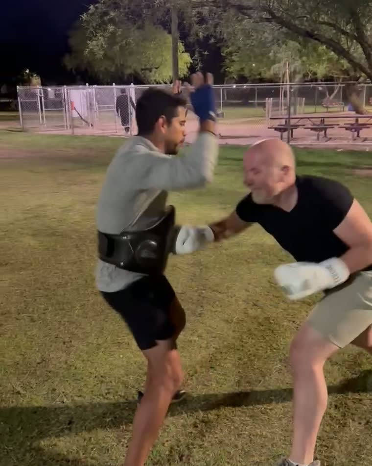 Two men sparring with gloves in a park at night